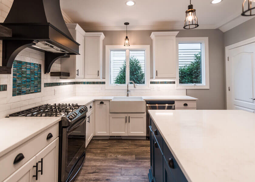 L-shaped white shaker kitchen with a navy blue island, white quartz worktops, farmhouse sink and black hardware