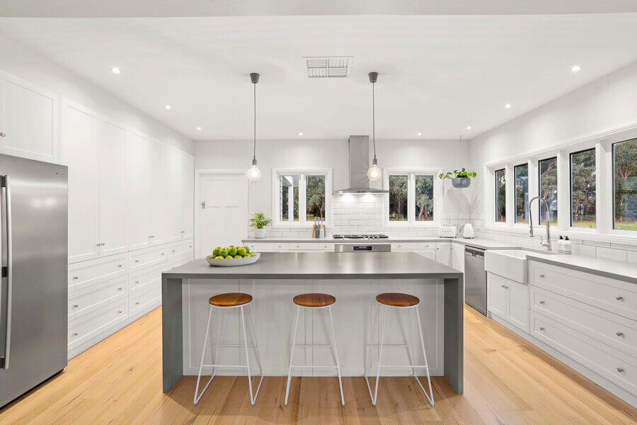 U-shaped white shaker kitchen with a grey waterfall island, three bar stools and light oak flooring